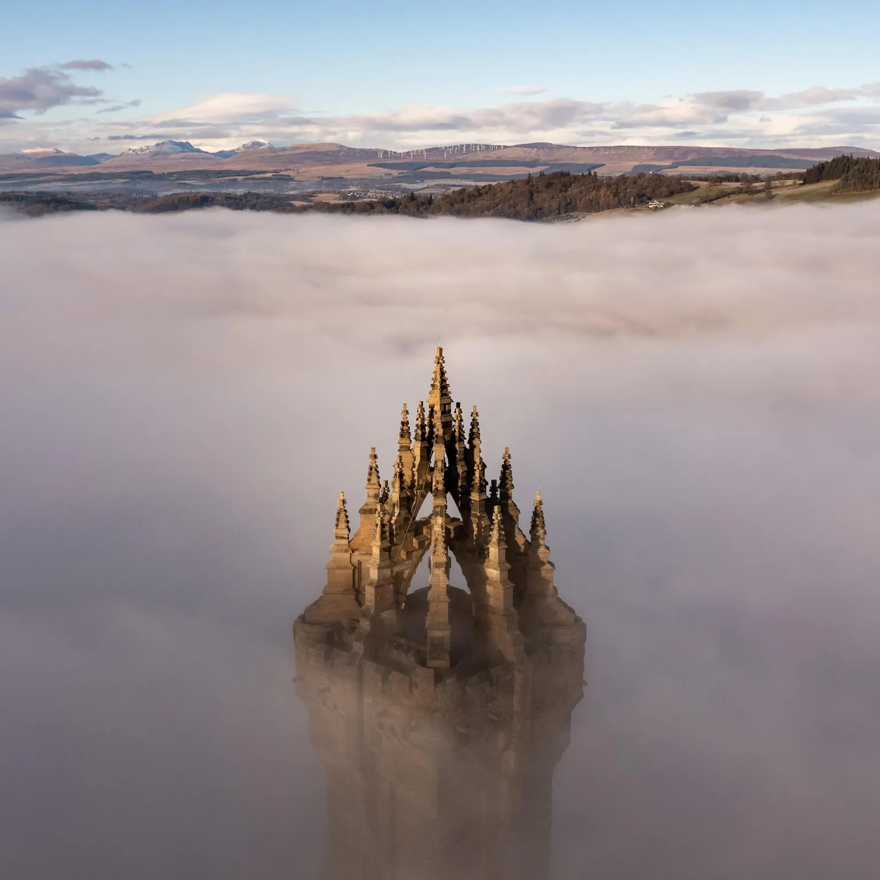 Top of Wallace Monument tower emerging from dense fog with Scottish hills and cloudy sky in background