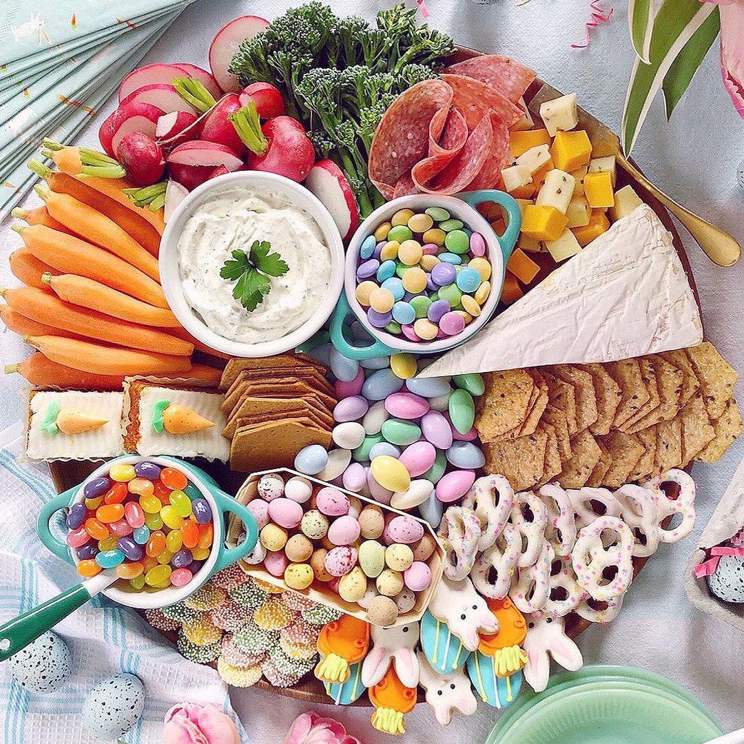 Easter charcuterie board with vegetables, meats, cheese, crackers, and colorful pastel candies on pink marble