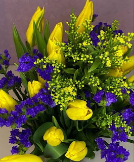 Bouquet of yellow tulips, purple statice, and green foliage with small yellow accent flowers