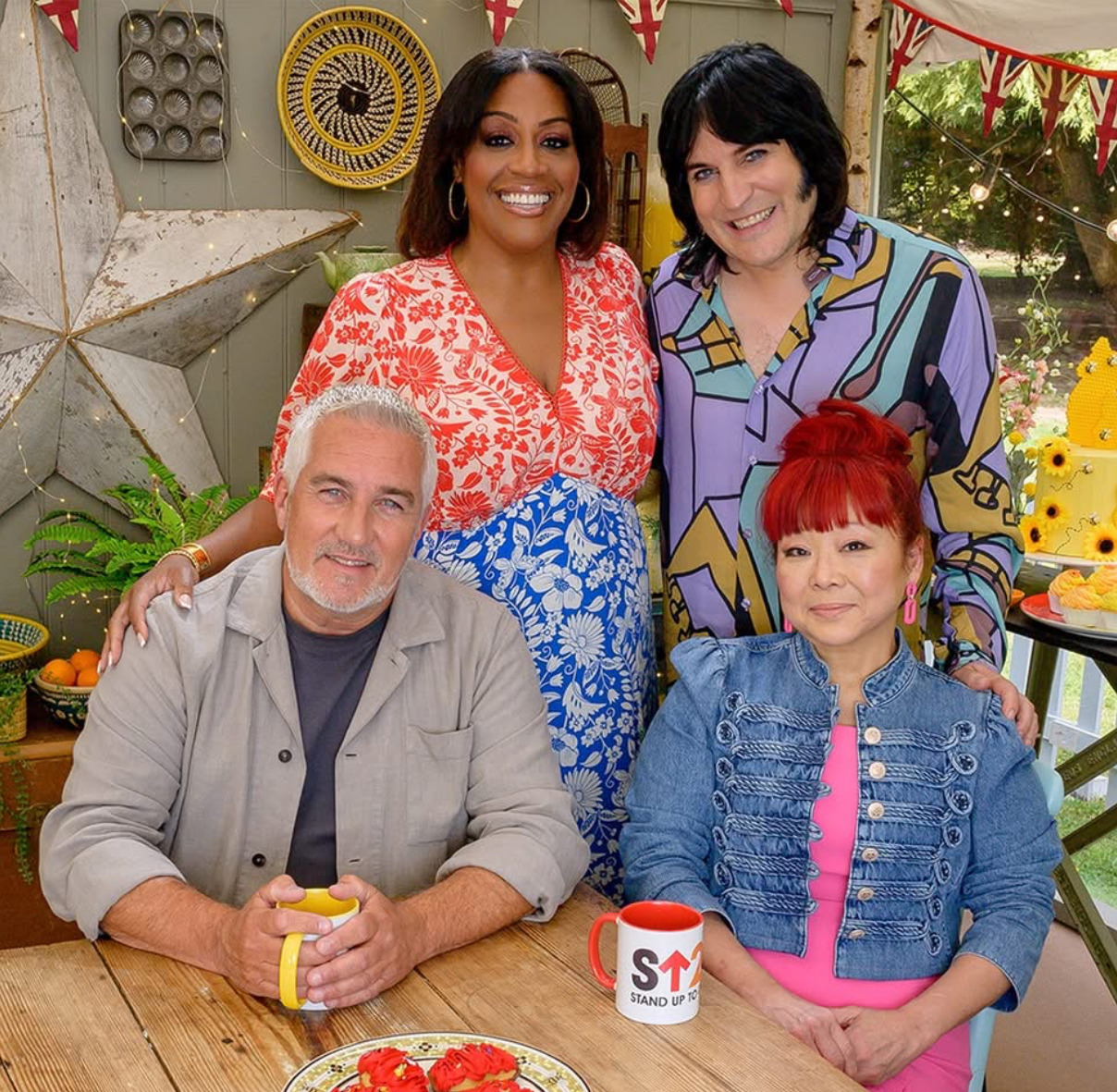 Four people posing together at a table in a colorful baking-themed indoor set