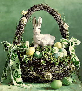 White ceramic bunny in woven twig basket with pastel eggs, flowers and green ribbons
