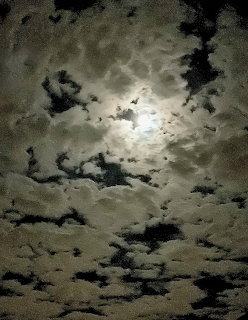 Full moon shining behind dense clouds in a dark night sky