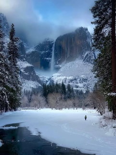 Snowy Yosemite Valley with Yosemite Falls, granite cliffs, pine trees, and a frozen river in winter