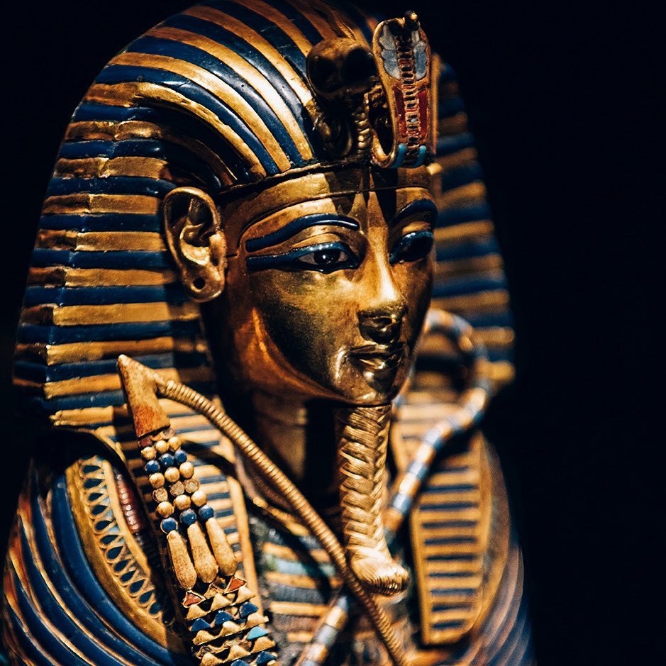 Golden funeral mask of Tutankhamun with striped blue headdress on black background