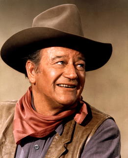 John Wayne smiling in brown cowboy hat and red bandana against tan background
