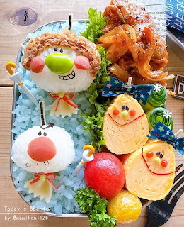Colorful bento box with cute kawaii food characters including rice balls with faces, fried food, and vegetable decorations