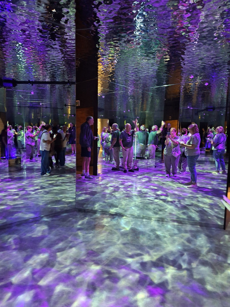 People standing inside a colorful immersive light installation with purple floor projections and hanging decorations