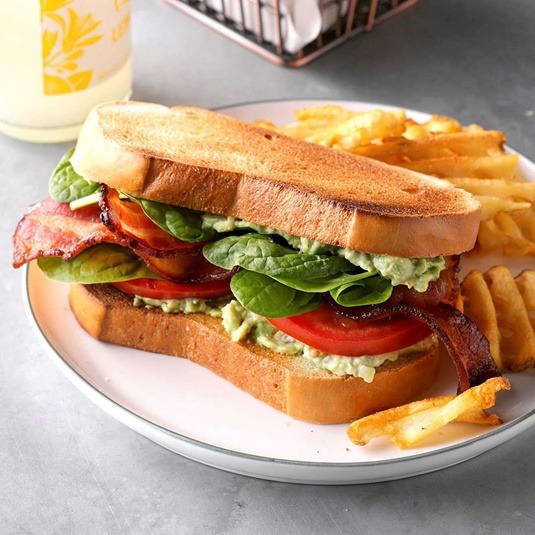 BLT sandwich with avocado on toasted bread served with fries on white plate