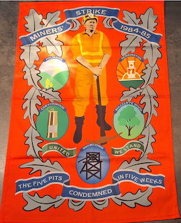Orange tea towel with a central miner figure, banners, and mining emblems