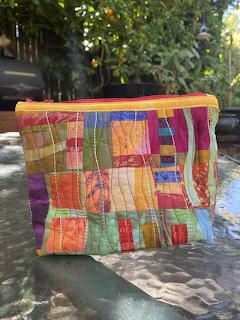 Colorful patchwork fabric pouch with quilted squares in bright colors on outdoor stone ledge