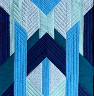 Geometric quilt in blue tones with chevron and diamond patterns