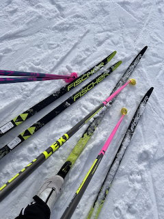 Cross country skis and poles in pink, yellow, and black laid out on snow