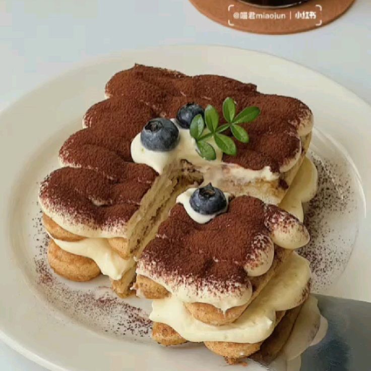 Tiramisu dessert with cocoa dusting, cream layers, blueberries and mint garnish