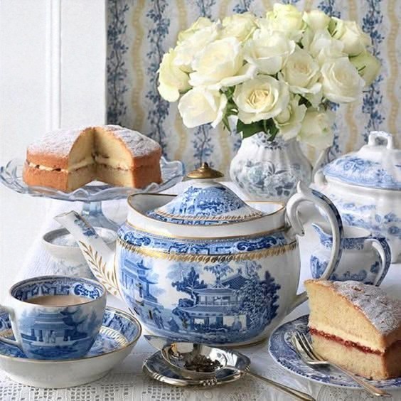 Blue and white tea set with sponge cake slices and white roses on a table