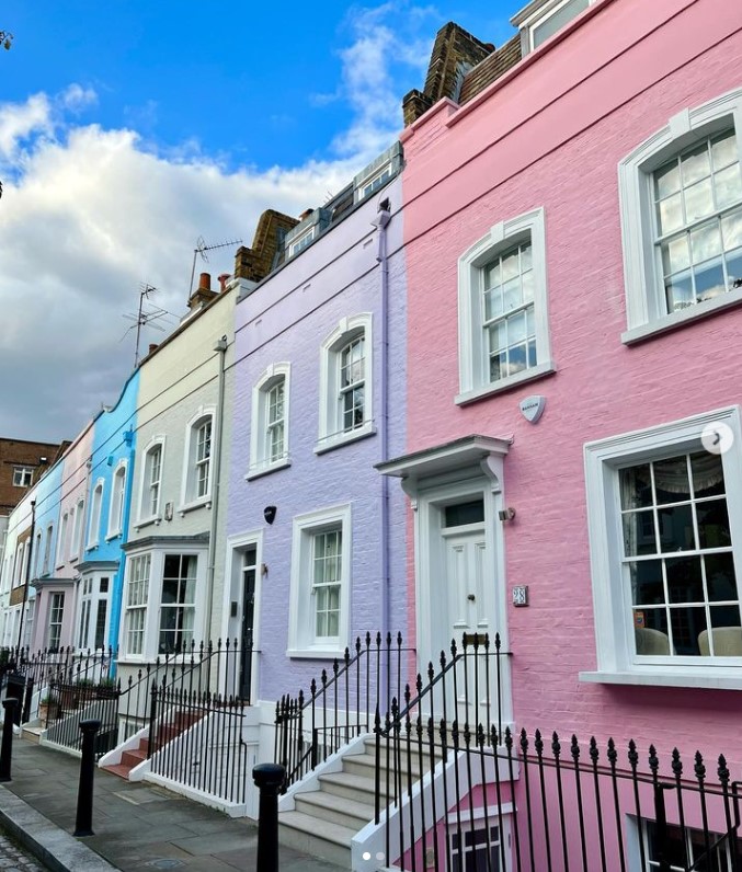 Row of pastel pink, blue and white townhouses with black iron railings under blue sky