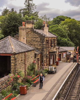 Old stone train station beside railway tracks with a platform and trees