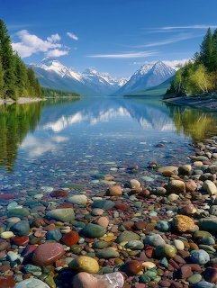 Colorful rocks in clear mountain lake with snow peaks and forest reflected in still water