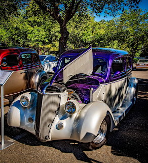 Purple and silver classic hot rod with open hood at an outdoor car show surrounded by trees