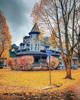 Victorian house with turret surrounded by autumn trees and fallen yellow leaves