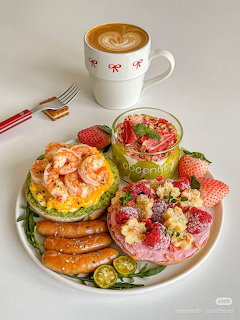Latte beside a brunch plate with waffles, sausages, fruit, shrimp toast, and colorful desserts