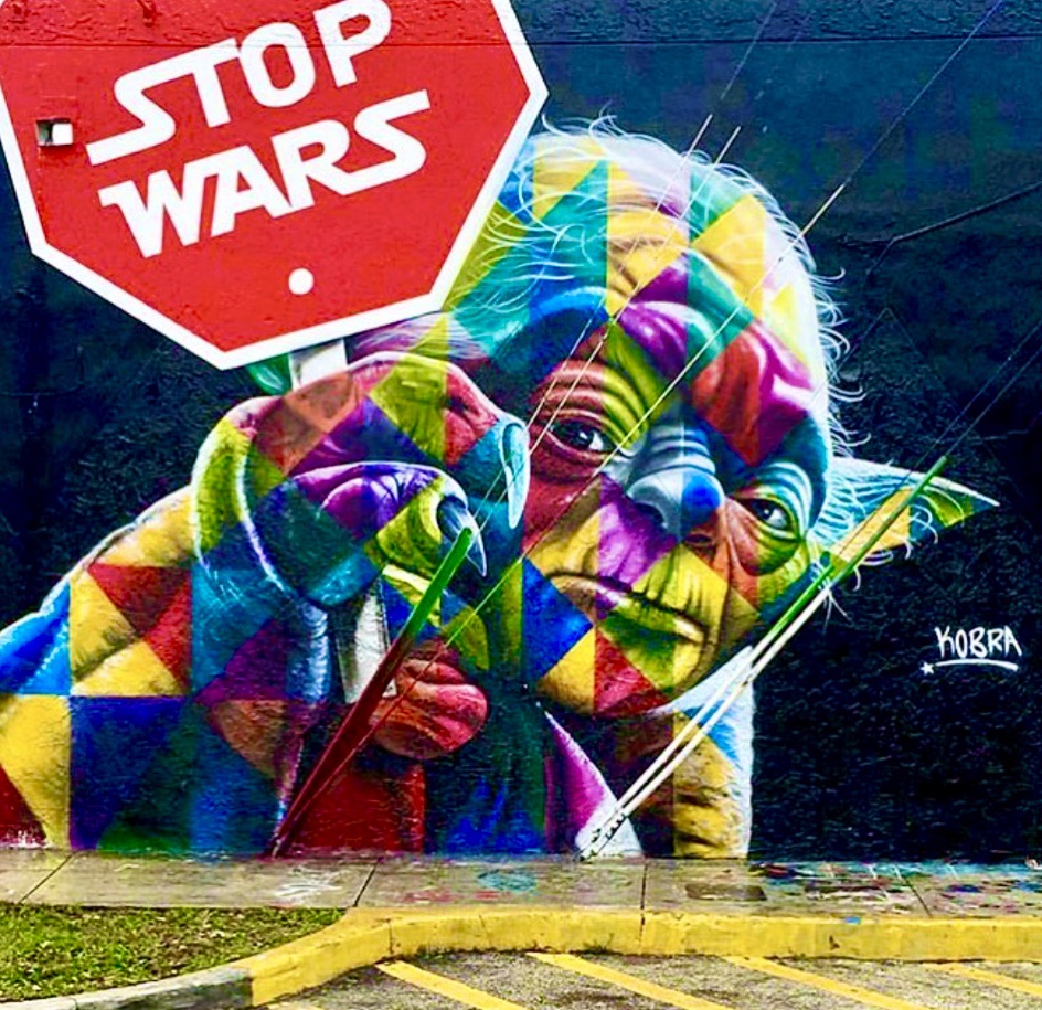 Colorful geometric street art mural of Yoda holding a lightsaber with a red Stop Wars sign