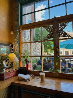 Sunlit cafe window with wooden frame, plants on sill, view of outdoor street scene