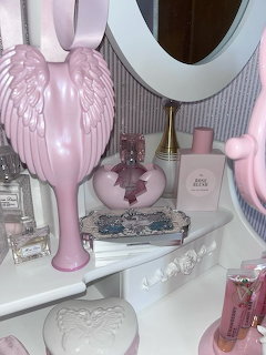 Pink vanity table with angel wing hairbrushes, perfume bottles, heart box, and feminine accessories
