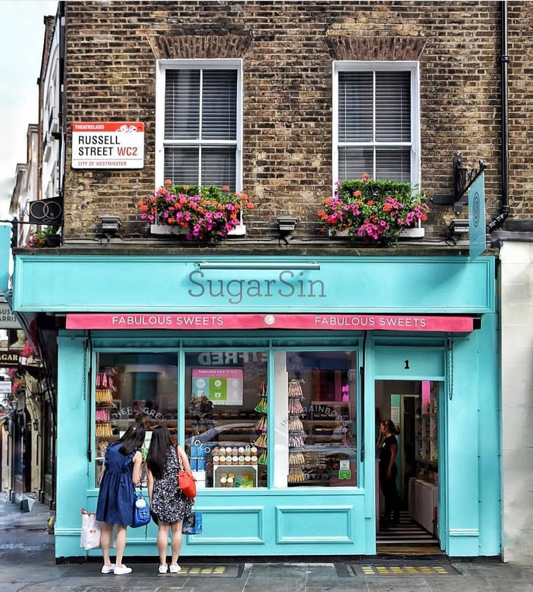 Turquoise candy shop storefront with pink flowers and brick building above