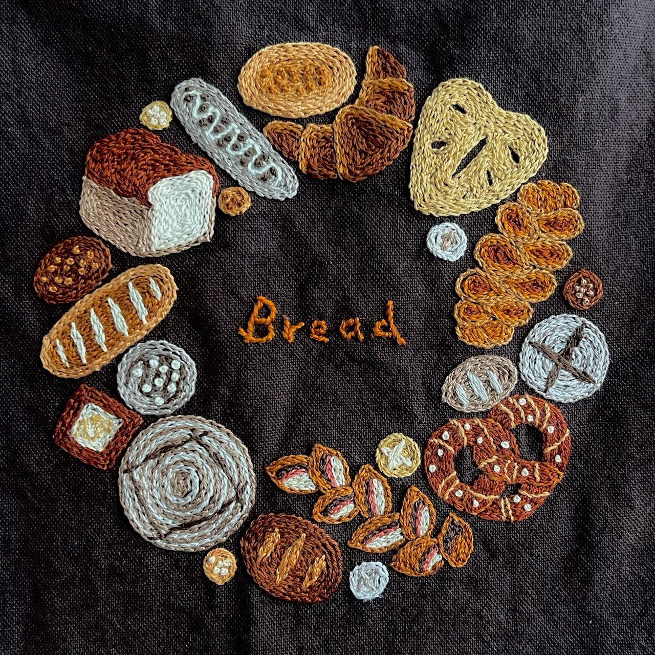 Embroidery of assorted breads and pastries arranged in a circle on dark fabric
