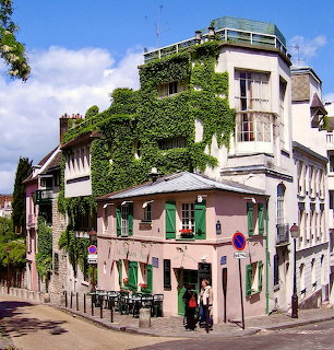 Pink building with green shutters on a Montmartre street corner, covered in ivy under blue sky