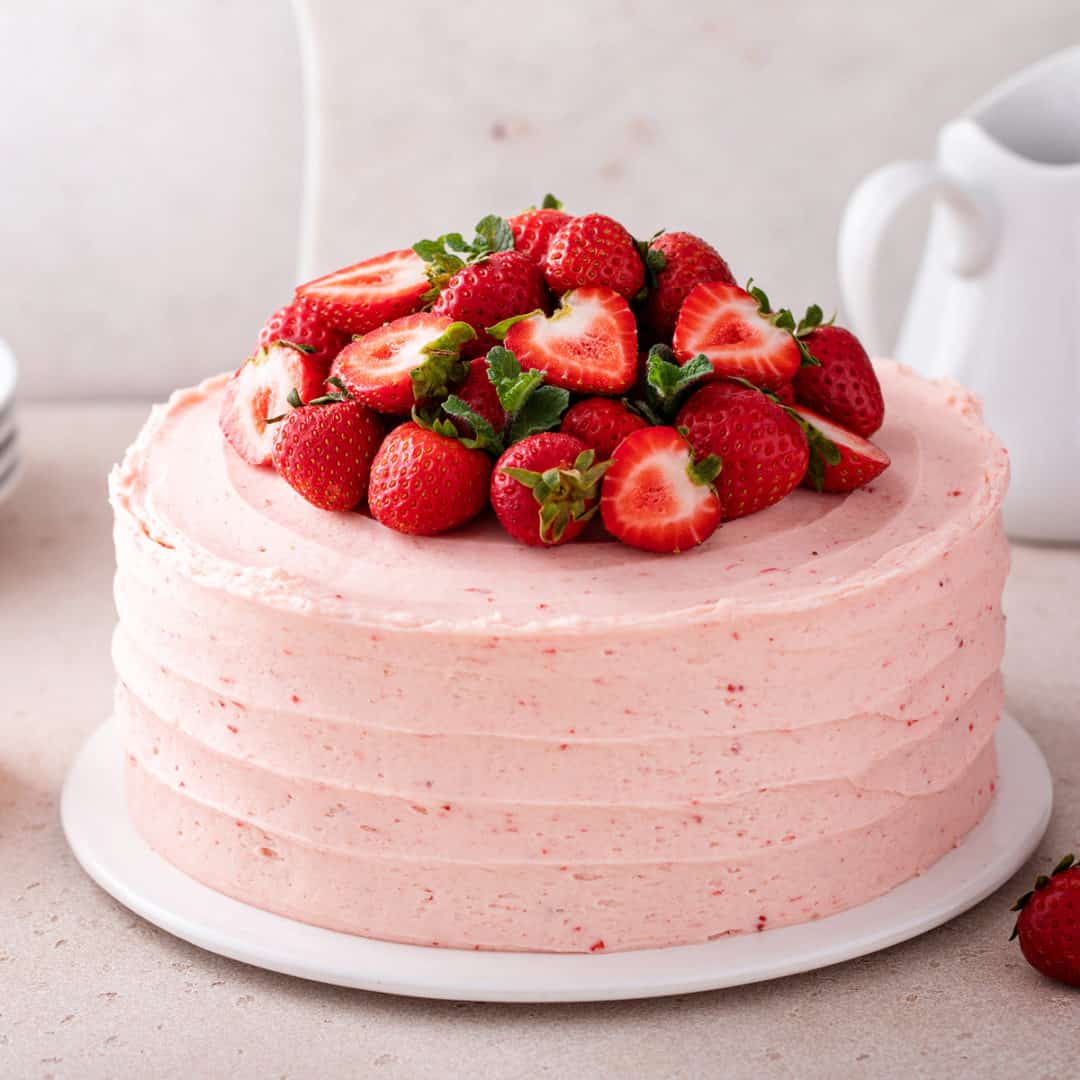 Pink frosted cake topped with fresh strawberries on a white cake stand
