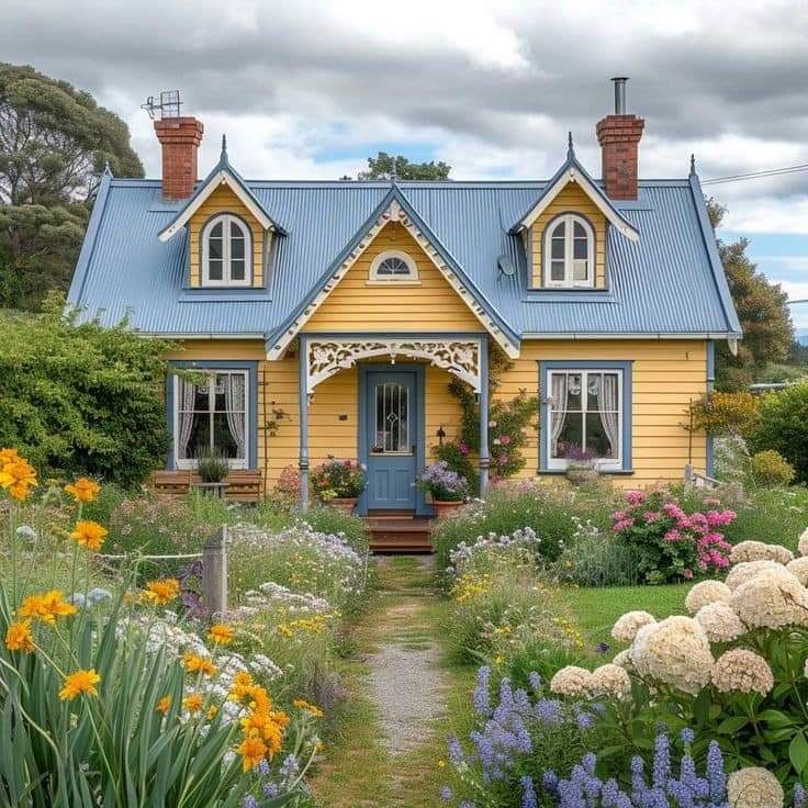 Yellow cottage with blue roof and vibrant flower garden in front