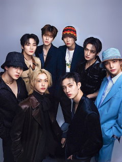 Eight young men in fashionable outfits posing together for a group studio portrait against a grey background