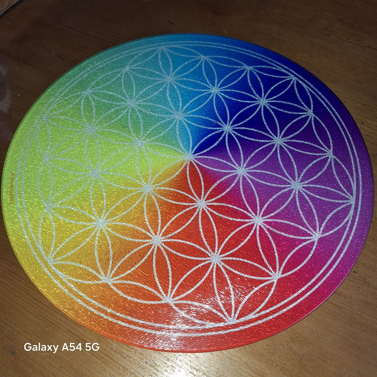 Circular rainbow gradient mandala with overlapping geometric flower pattern on wooden surface