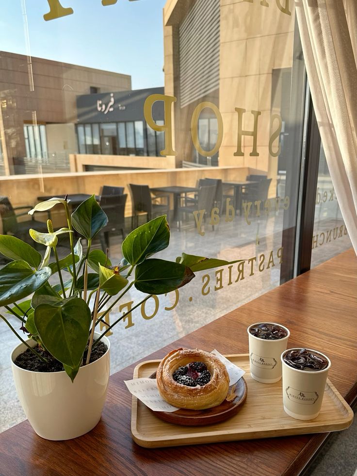 Two iced americano coffees and a danish pastry on a cafe table by a window