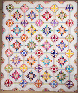 Handmade quilt with colorful geometric star blocks in grid layout on white fabric with floral border