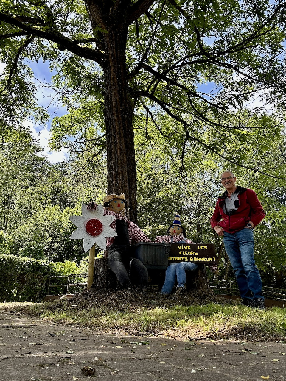 Three people sitting on a bench under a large tree in a sunny park