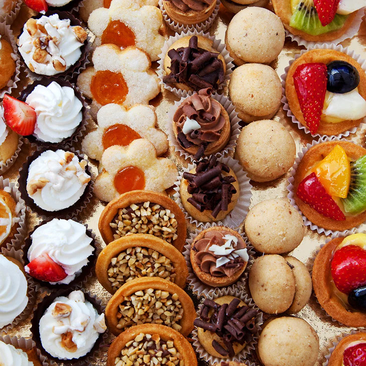 Overhead view of assorted miniature French pastries with fruit, cream, and chocolate toppings