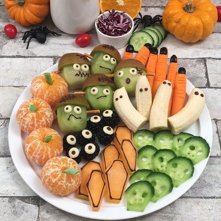Halloween fruit platter with decorated apples, bananas, kiwis, and oranges arranged on white plate with pumpkins