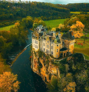 Aerial view of Walzin Castle on a cliff overlooking a river bend, surrounded by autumn foliage and green fields