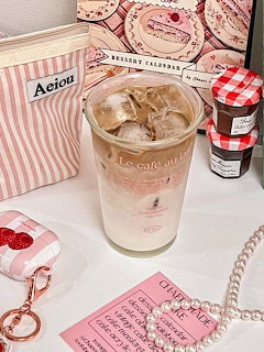Iced coffee in glass on pink striped table with feminine accessories and cherry decorations