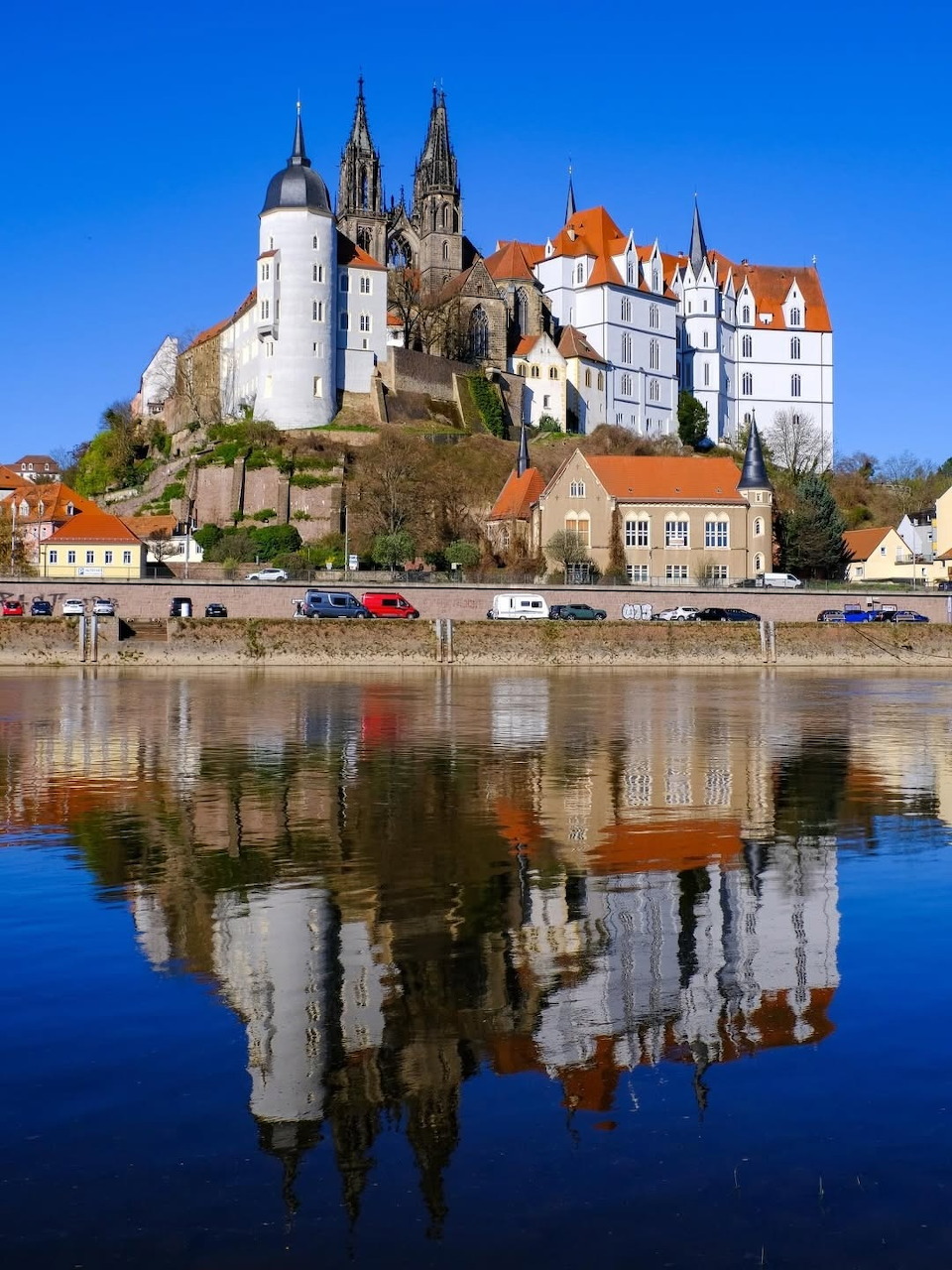 Medieval castle on hill with Gothic spires reflected in river