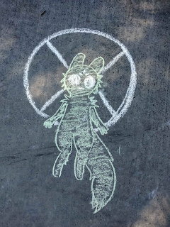 Chalk drawing of a winged cat character with big eyes and a circle divided into sections on pavement