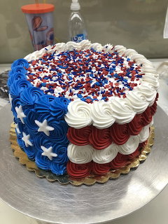 Round red, white, and blue cake with piped frosting, white stars, and red-blue sprinkles