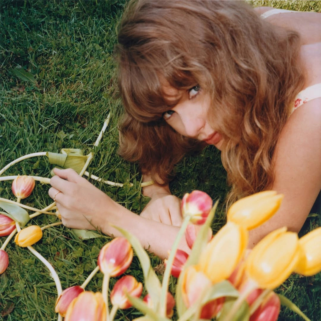 Young woman lying on grass near tulips, holding a drink outdoors