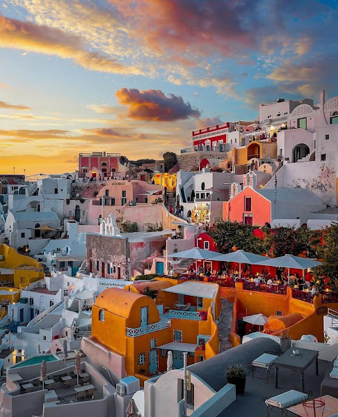 Santorini white buildings with blue domes at sunset, colorful sky over Greek island village