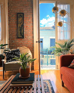 Sunlit living room with brick wall, city view through balcony door, plants and orange couch
