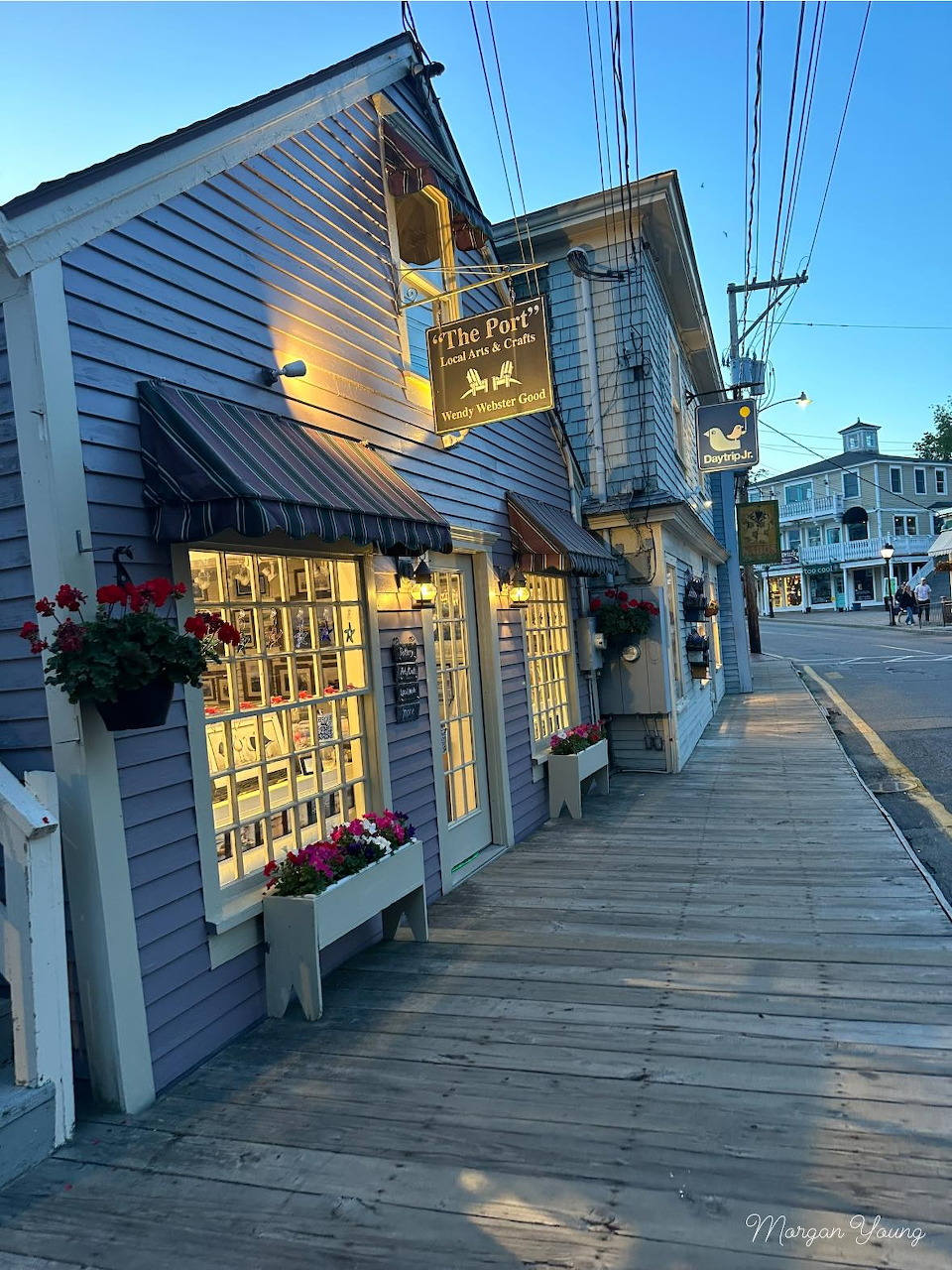 Lit wooden storefront on a boardwalk in Kennebunkport, Maine, at evening with flower boxes and awnings