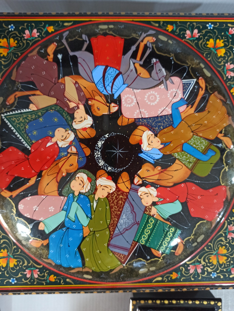 Persian miniature painting showing people in traditional dress within decorated circular frame with floral border