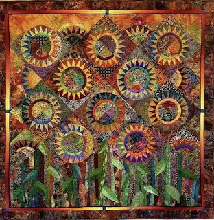 Colorful quilted artwork showing multiple patchwork sunflowers with green stems against an orange-red textured background
